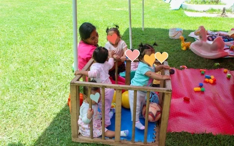 Cuidadora con bebés jugando dentro de un corral de madera en el jardín