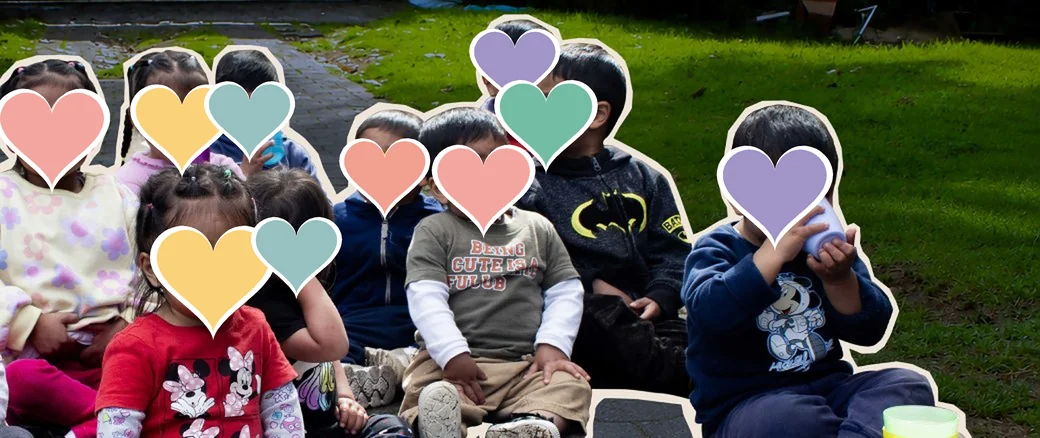 Niñas y niños del Hogar sentados en el jardín, con los rostros cubiertos por corazones