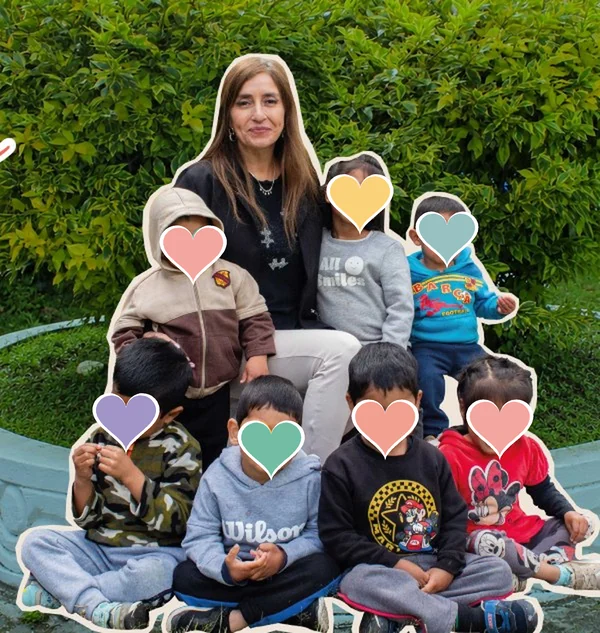 La directora del Hogar junto a niñas y niños en el jardín, con los rostros cubiertos por corazones