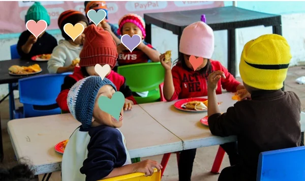 Niñas y niños con gorros de lana comiendo juntos en el comedor