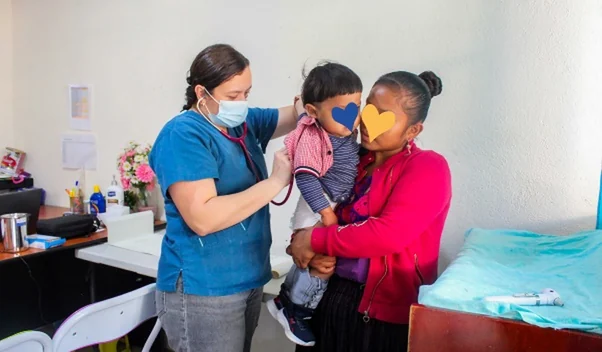 Doctora revisando con estetoscopio a un niño en brazos de su cuidadora